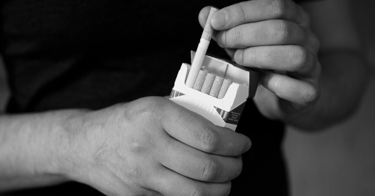 A monochrome close-up of hands holding a cigarette pack, emphasizing addiction.